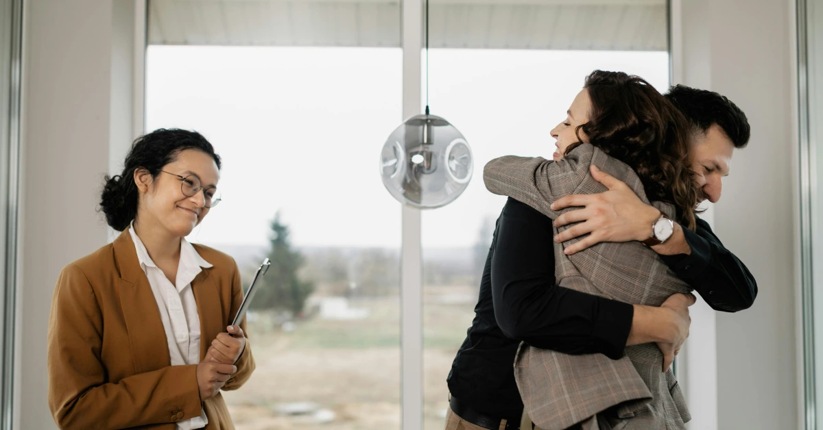 A Couple Hugging Each Other Beside a Real Estate Agent